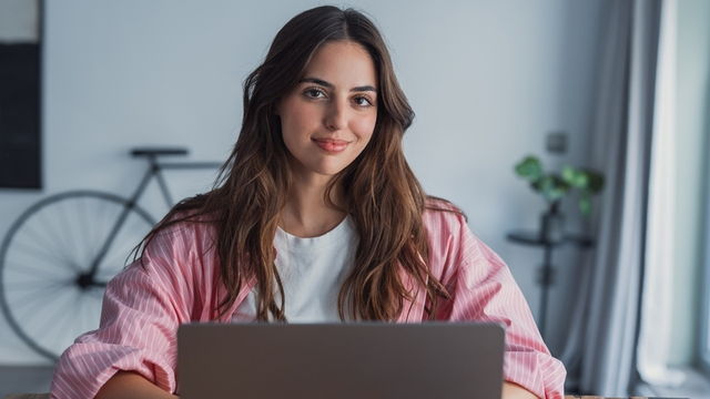 Una estudiante sonríe, mientras usa su ordenador portátil desde una oficina o desde su casa