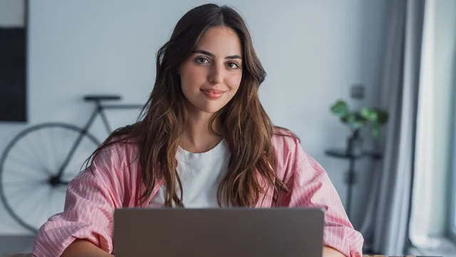 Una estudiante sonríe, mientras usa su ordenador portátil desde una oficina o desde su casa