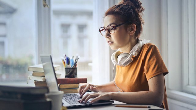 chica con gafas sentada frente a un ordenador portátil y llevando unos auriculares en el cuello