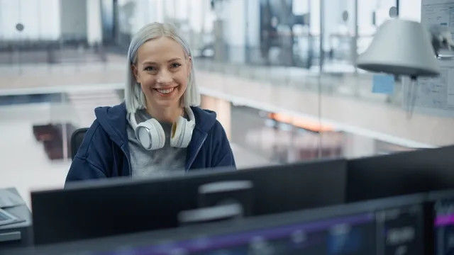Sonriente ingeniera de software con auriculares, trabajando en un desarrollo en una oficina moderna