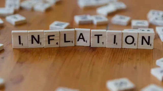 The word "INFLATION" spelled out with wooden letter tiles on a brown wooden surface