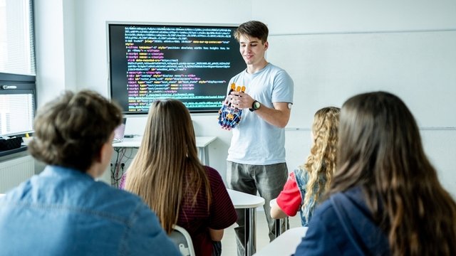 Muchacho adolescente que presenta un proyecto robótica delante de sus compañeros