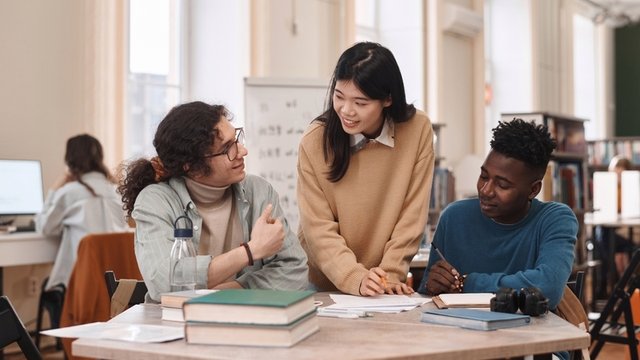 tres estudiantes haciendo un intercambio de idiomas en una biblioteca