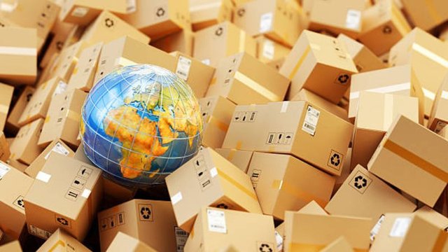 A small glass globe showing Europe and Africa sits atop a massive pile of cardboard shipping boxes, representing global commerce and international shipping logistics.