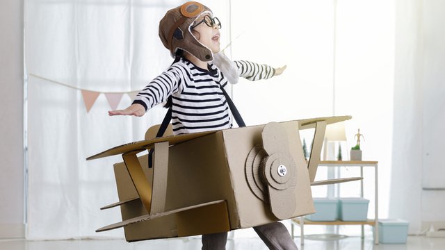 niña jugando con un avión hecho de cartón