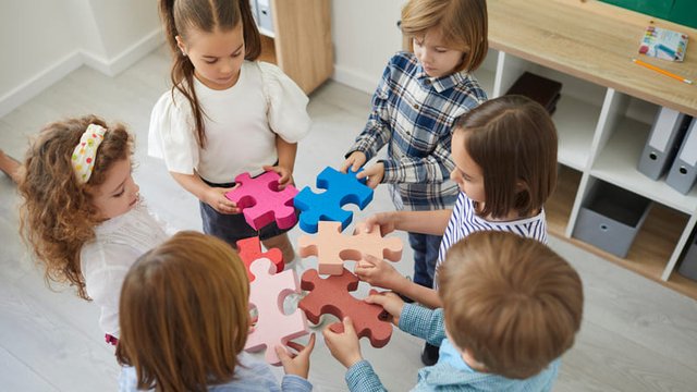 estudiantes de Primaria en círculo sosteniendo piezas de colores de un rompecabezas