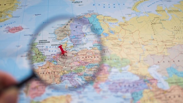 una chincheta roja, bajo una lupa, señala una ciudad de Alemania en un mapa de colores