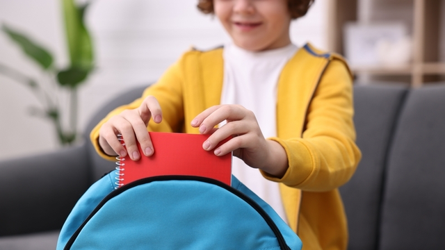 Muchacho que embala su mochila para la escuela en el sofá en casa, primer plano