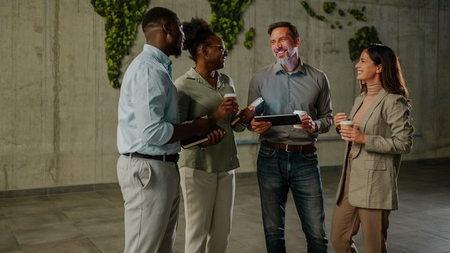 Diversos colegas de negocios que trabajan en red y colaboran durante una pausa para el café en una oficina moderna con un mapa del mundo verde en la pared