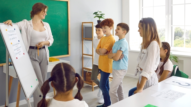 maestra muestra a sus estudiantes un cartel que tiene escritas las normas de convivencia en el aula