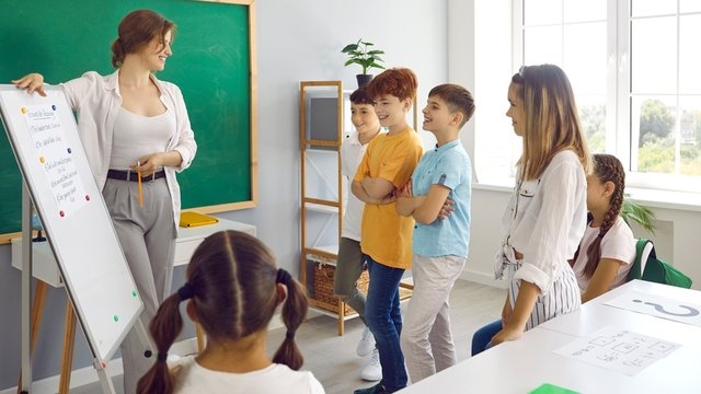 maestra muestra a sus estudiantes un cartel que tiene escritas las normas de convivencia en el aula