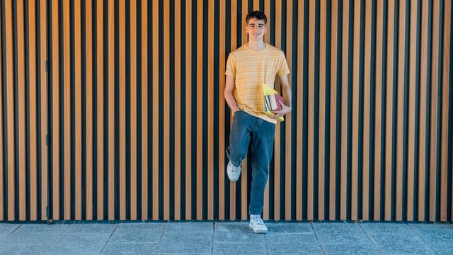 estudiante adolescente sostiene varios libros y apoya el pie en la pared