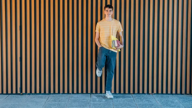estudiante adolescente sostiene varios libros y apoya el pie en la pared