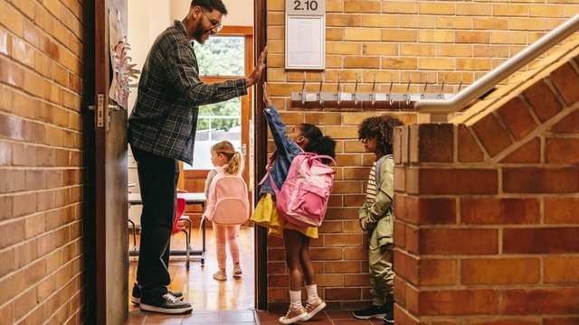 profesor de primaria saludando a sus alumnos en la puerta