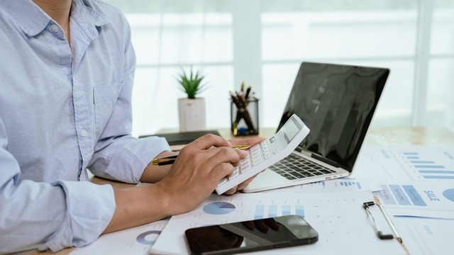 persona de negocios trabajando con una calculadora en un escritorio repleto de informes financieros y gráficos