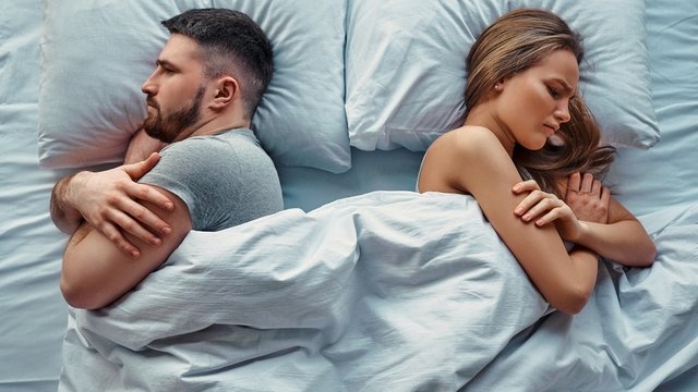 pareja tumbada en la cama con los brazos cruzados y expresión de enfado