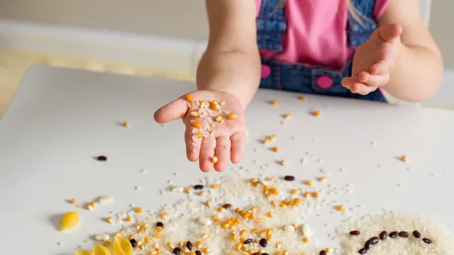 Las manos de una niña pequeña jugando con arroz, palomitas de maíz, judías pintas y pasta