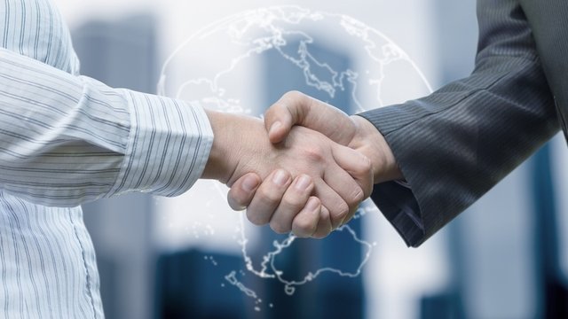 Dos personas se dan la mano. Una de ellas va en mangas de camisa y la otra lleva puesta la chaqueta de un traje