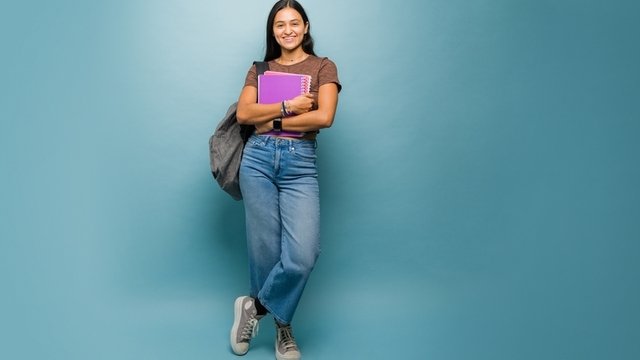 estudiante universitaria sosteniendo unas libretas y sonriendo