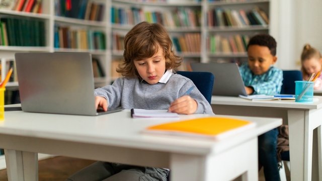 niños de Educación Primaria sentados frente a ordenadores portátiles en un aula de informática