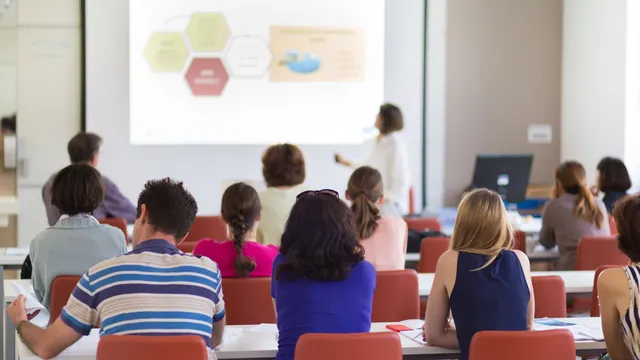 estudiantes en un aula atendiendo las explicaciones de una persona docente