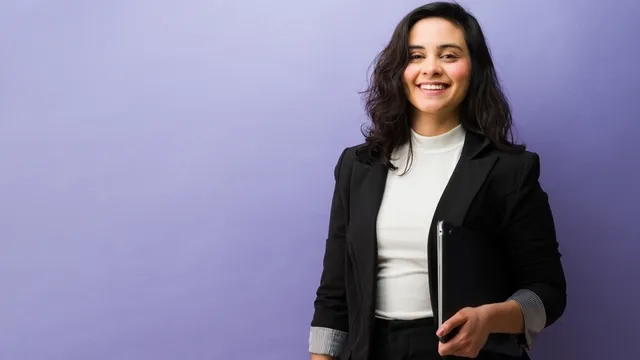 Chica sonriendo, de pie sobre fondo púrpura con una tableta digital, que representa la confianza y el éxito