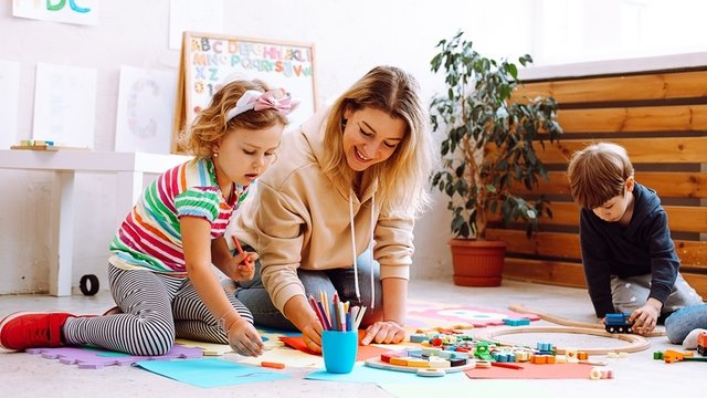 maestra de Educación Infantil realizando una tarea con sus estudiantes sentada en el suelo del aula