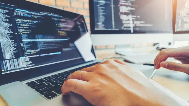 persona trabaja con un portátil y una segunda pantalla con un lenguaje de programación