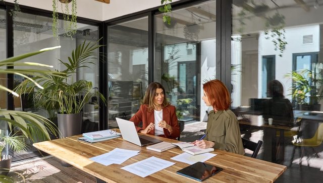 auxiliar administrativa y gerente mantienen una conversación de trabajo, mientras usan un ordenador portátil