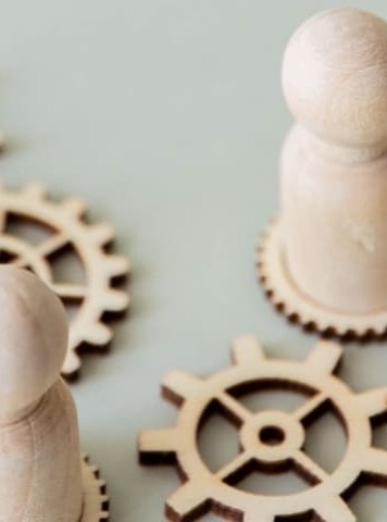 una imagen conceptual con figuras de madera de pie sobre engranajes interconectados