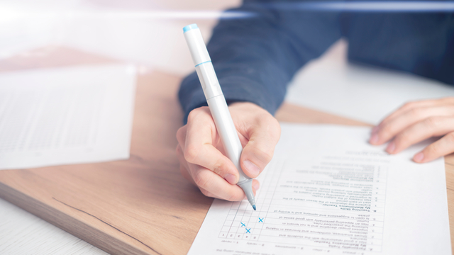 primer plano de las manos de una persona escribiendo con un rotulador de tinta azul en una hoja de papel