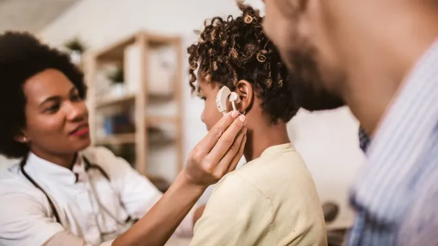 técnica en audiología protésica interactúa con uno niño y su padre