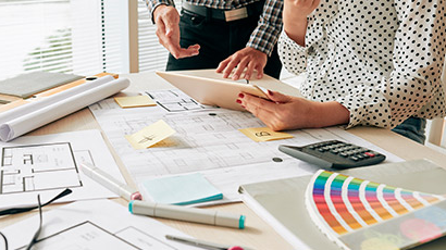 Dos personas revisando planos y documentos de dise&ntilde;o, trabajando en un proyecto arquitect&oacute;nico sobre una mesa