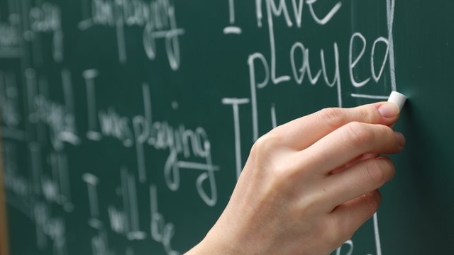 primer plano de la mano de un profesor de inglés escribiendo con tiza en una pizarra verde