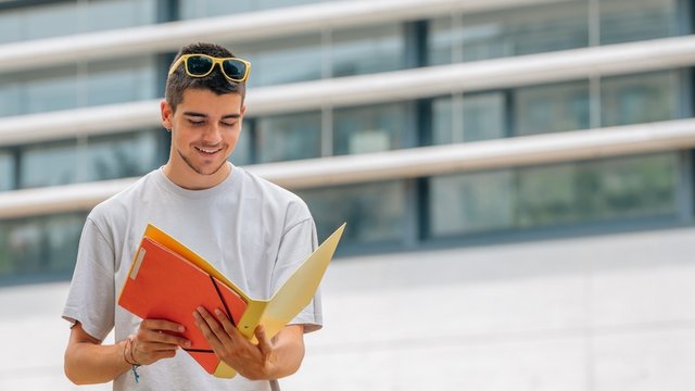 estudiante leyendo unos documentos que se encuentran dentro de una carpeta que sostiene entre manos