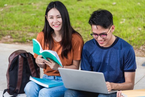 Two college students studying together outdoors with a laptop and books