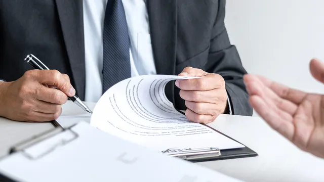 persona vestida con traje de chaqueta revisa un contrato de trabajo antes de firmarlo