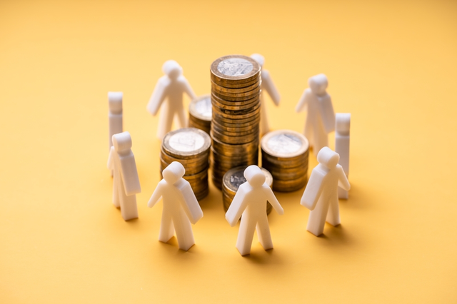 Figuras de personas blancas rodeando pilas de monedas doradas sobre fondo amarillo, representando el concepto de crowdfunding y financiaci&oacute;n colectiva