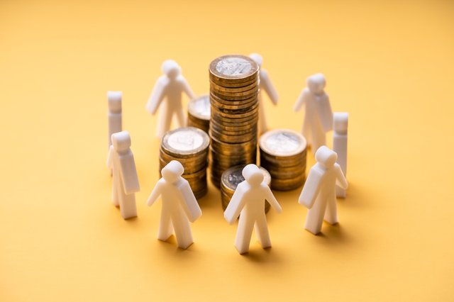 Figuras de personas blancas rodeando pilas de monedas doradas sobre fondo amarillo, representando el concepto de crowdfunding y financiación colectiva