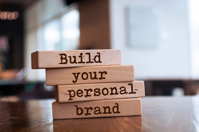Bloques de madera apilados con el texto "Build your personal brand" sobre escritorio, representando la construcci&oacute;n de marca personal para emprendedores