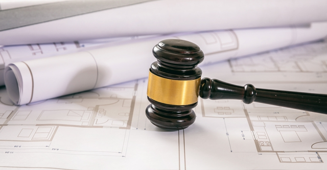 Mazo de juez sobre planos arquitectónicos, representando el derecho urbanístico y la regulación legal de la construcción