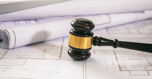 Mazo de juez sobre planos arquitectónicos, representando el derecho urbanístico y la regulación legal de la construcción