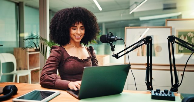 Periodista mujer trabajando con ordenador portátil, micrófono y tablet para producción de contenido digital