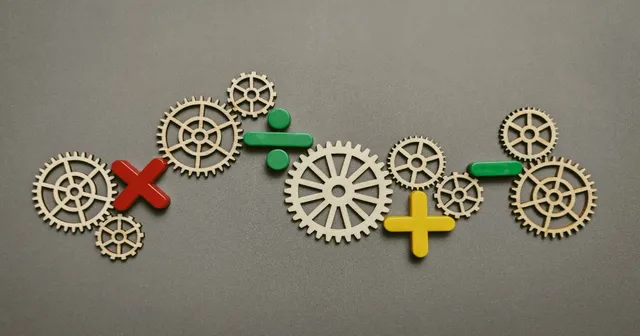 Wooden cogs interconnected with plastic math signs on a gray surface.