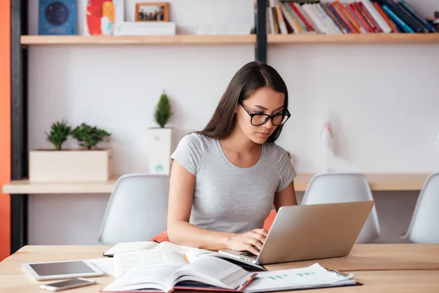 Mujer joven estudiando una maestria en su ordenador, entre libros