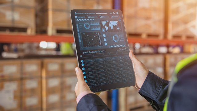 unas manos sostienen una tableta donde se puede ver la interfaz de un software logístico