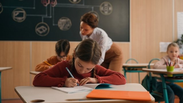 clase de un colegio en la que una profesora ayuda a sus alumnos mientras estudian