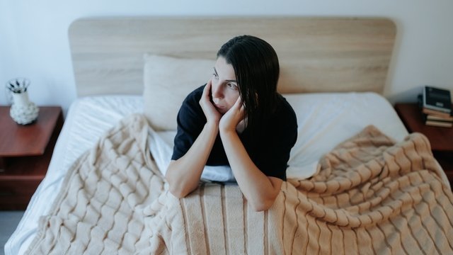 chica joven sentada en su cama con semblante serio y triste