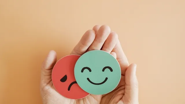 manos que sostienen chapas con los iconos de felicidad y tristeza