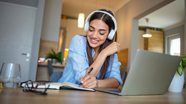 estudiante universitaria sentada a la mesa en casa usando ordenador portátil y auriculares mientras estudia